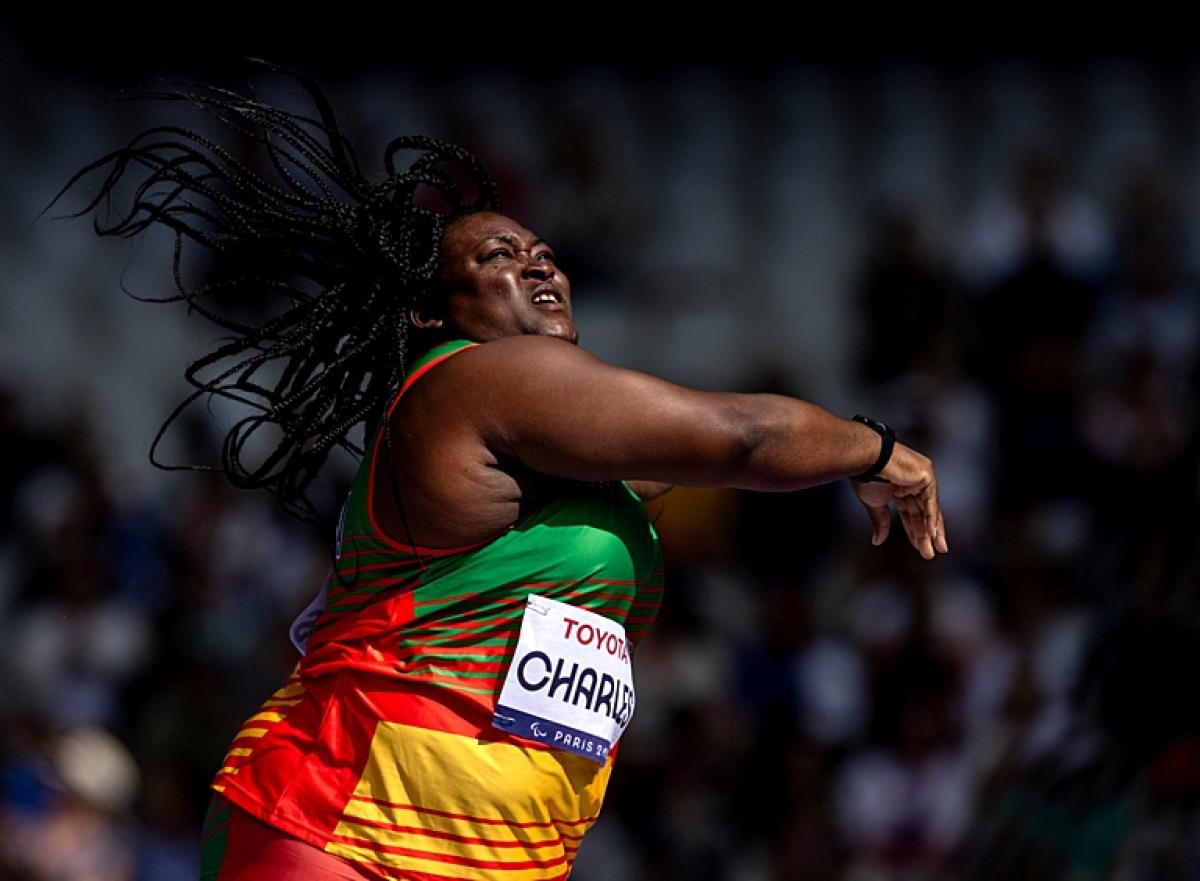 A female athlete wearing a red, yellow and green uniform is throwing