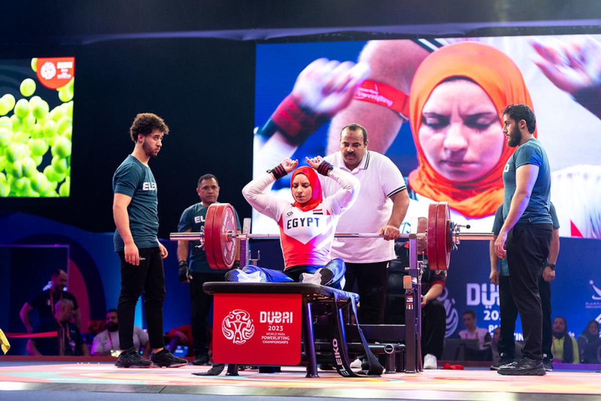 A female powerlifter on the bench observed by the coach and three loaders