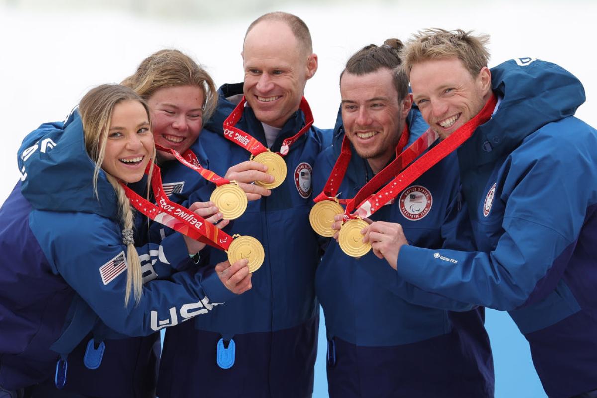 Five athletes pose for a photo while holding gold medals