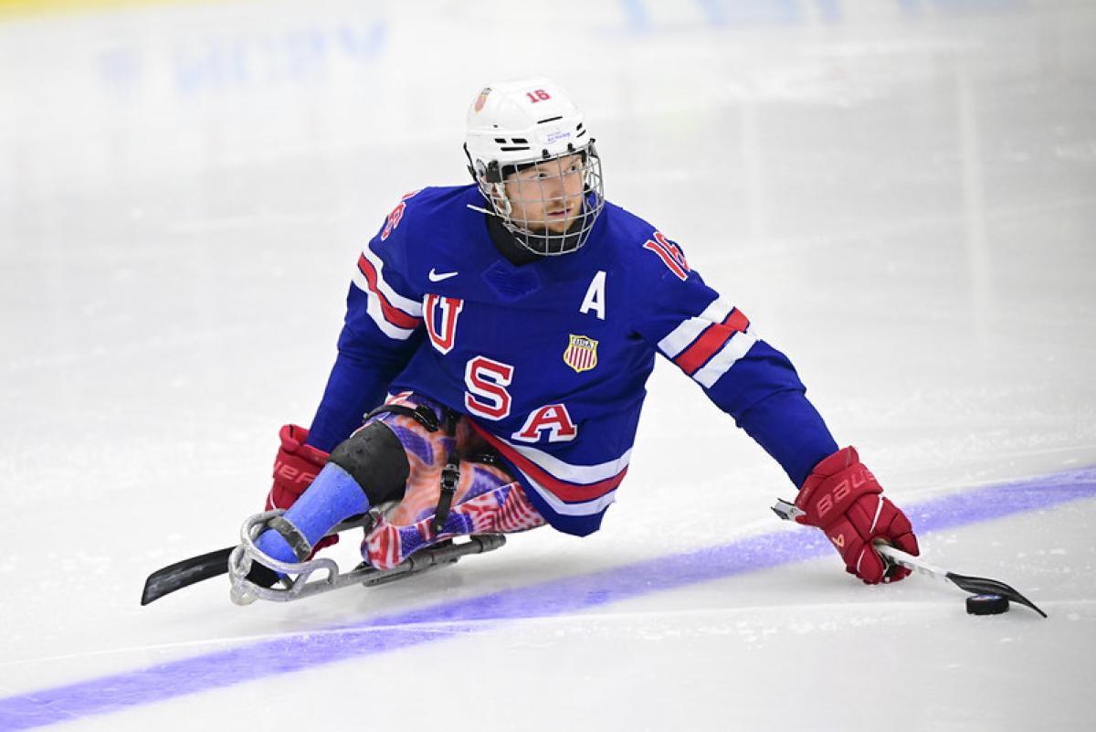 A male Para ice hockey player, who is wearing a blue Team USA kit and helmet, is in action