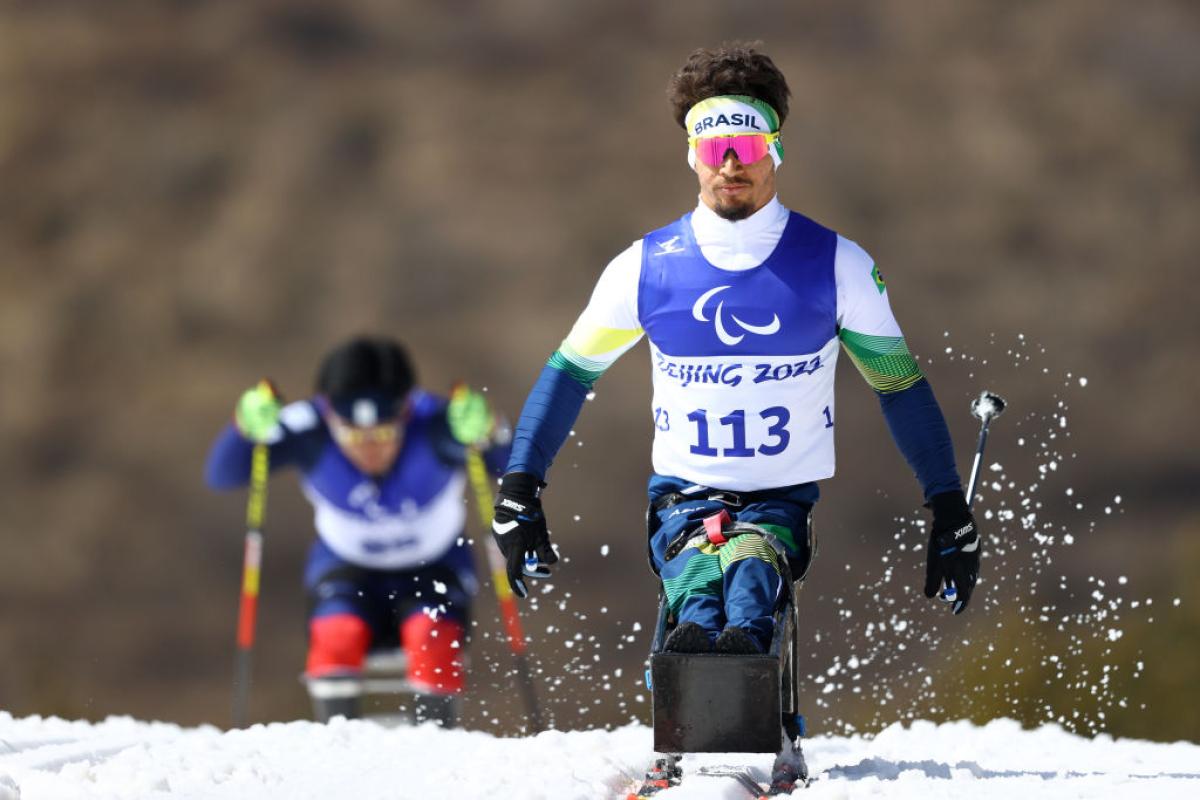 A male Para athlete competing in Para cross-country skiing on a sit-ski