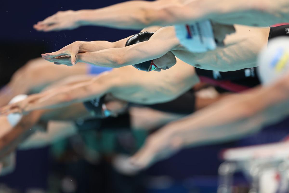 A group of male swimmers jumping into the pool at the start of a race