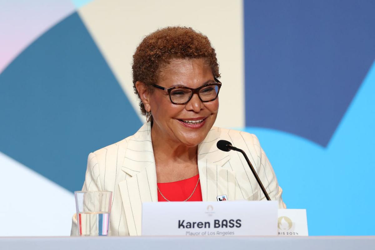Mayor Karen Bass speaks during a Paris 2024 press conference. She is sitting in front of a mic and a name tag