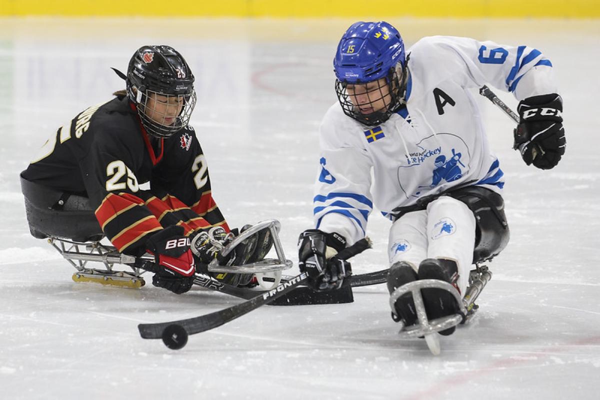 A Canadian player challenging a Team World player in a women's Para ice hockey game