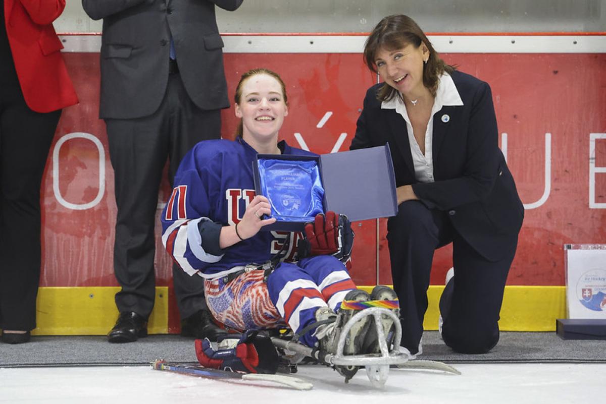 A female Para ice hockey player receiving an award next to a woman on the ice