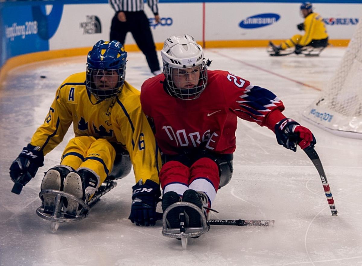 A Norwegian female Para ice hockey player in a challenge with a Swedish male player