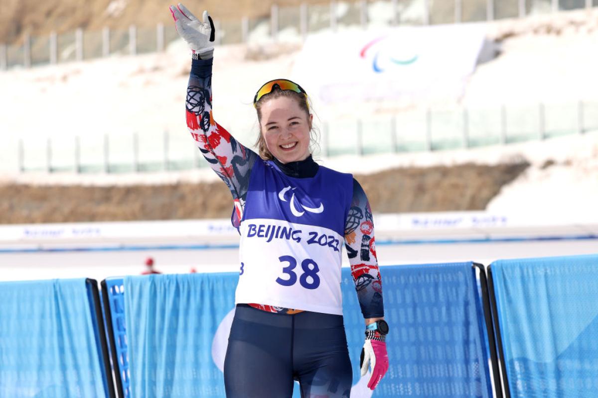A female skiing athlete is waving after her race
