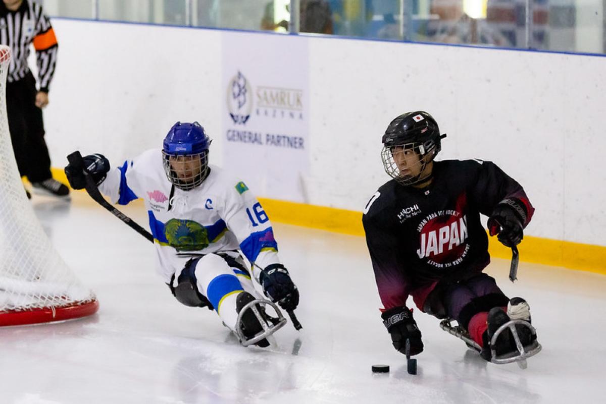 A Japanese Para ice hockey player with the puck with a Kazak player behind him