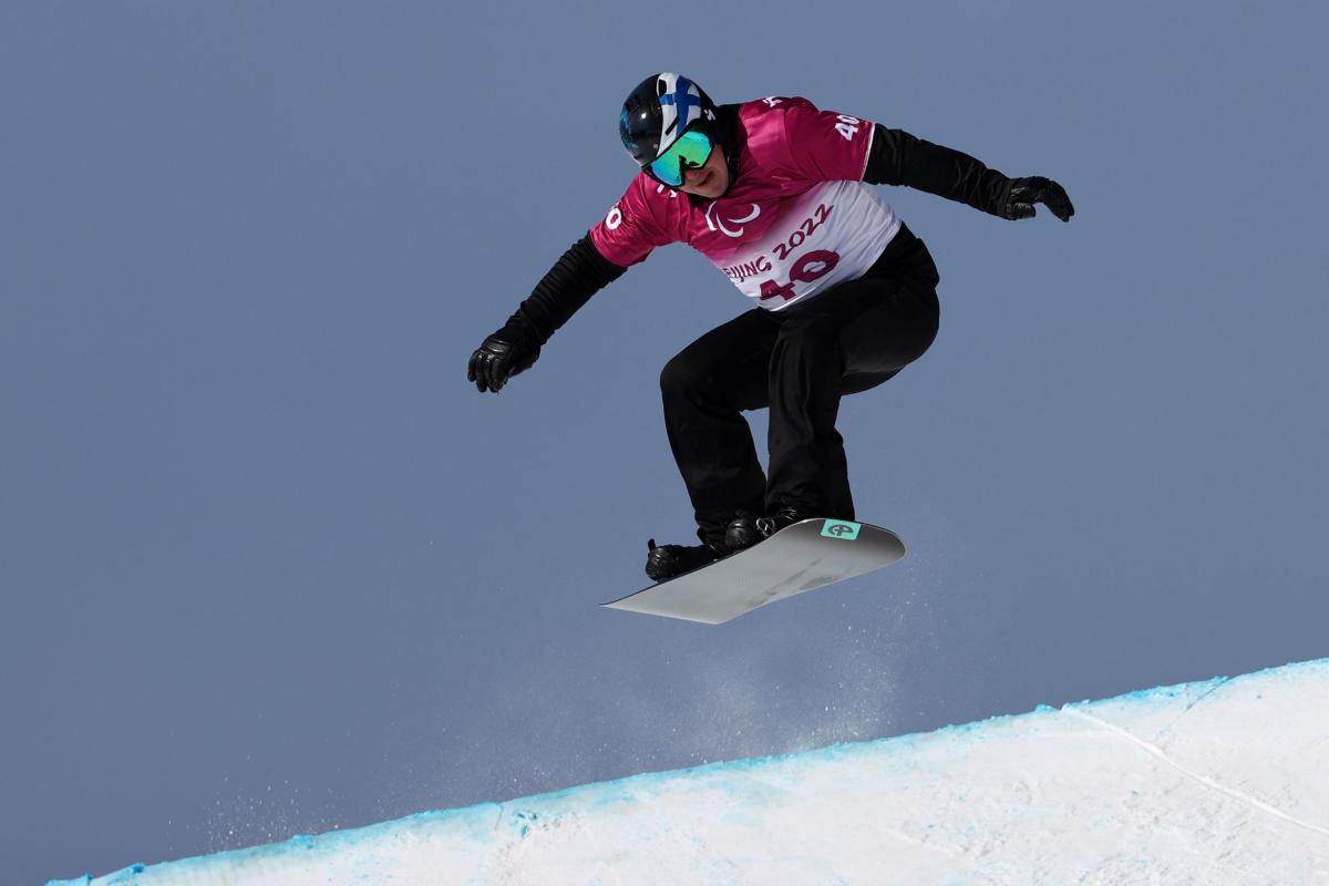 A male Para snowboarding athlete is in the air during a competition