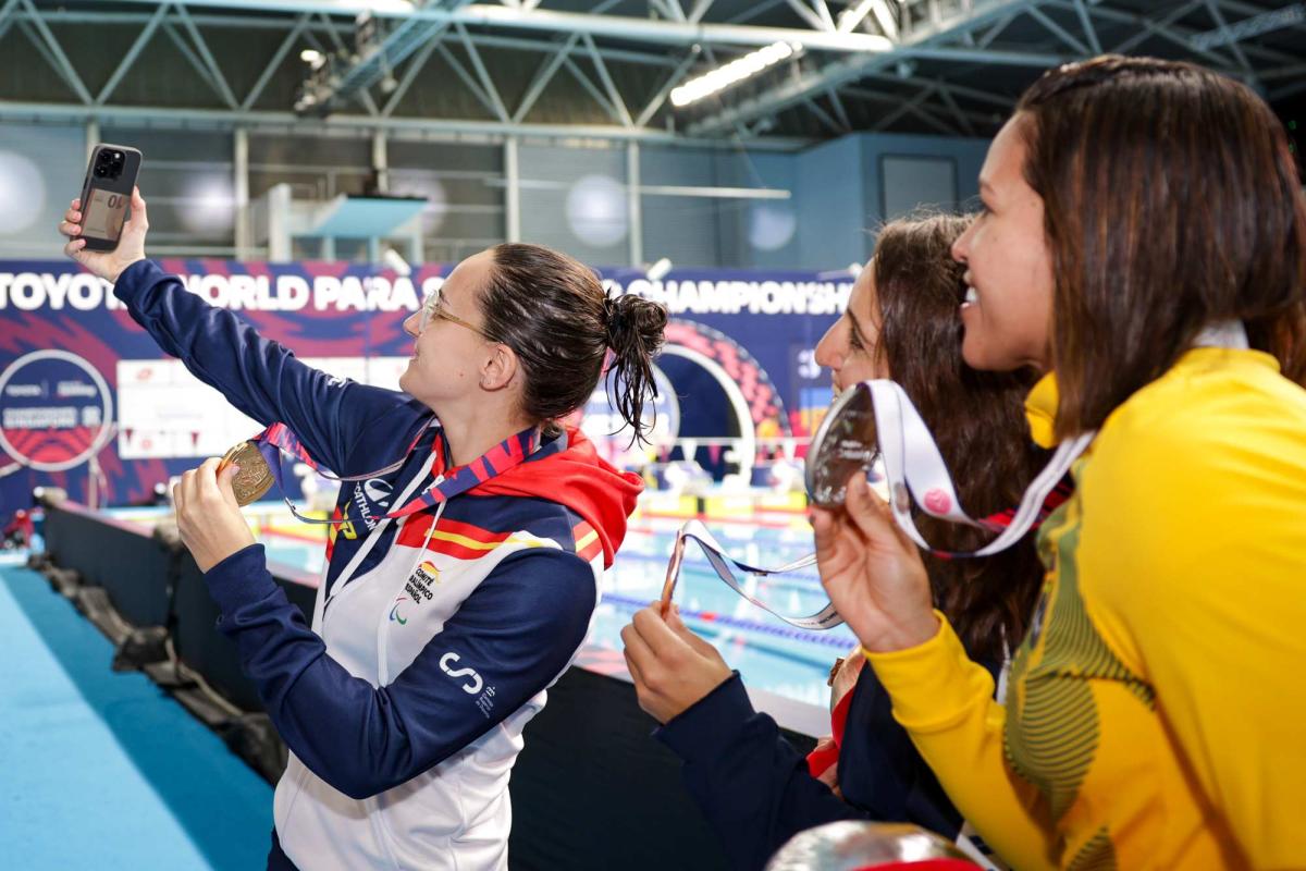 A young woman taking a selfie with two other women showing their medals