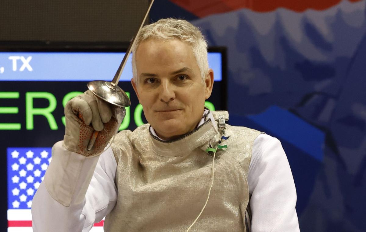 Scott Rodgers smiles for a photo while holding an epee