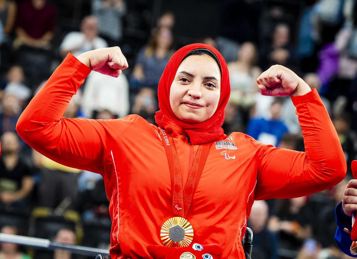 A female athlete with a gold medal flexing her arms 