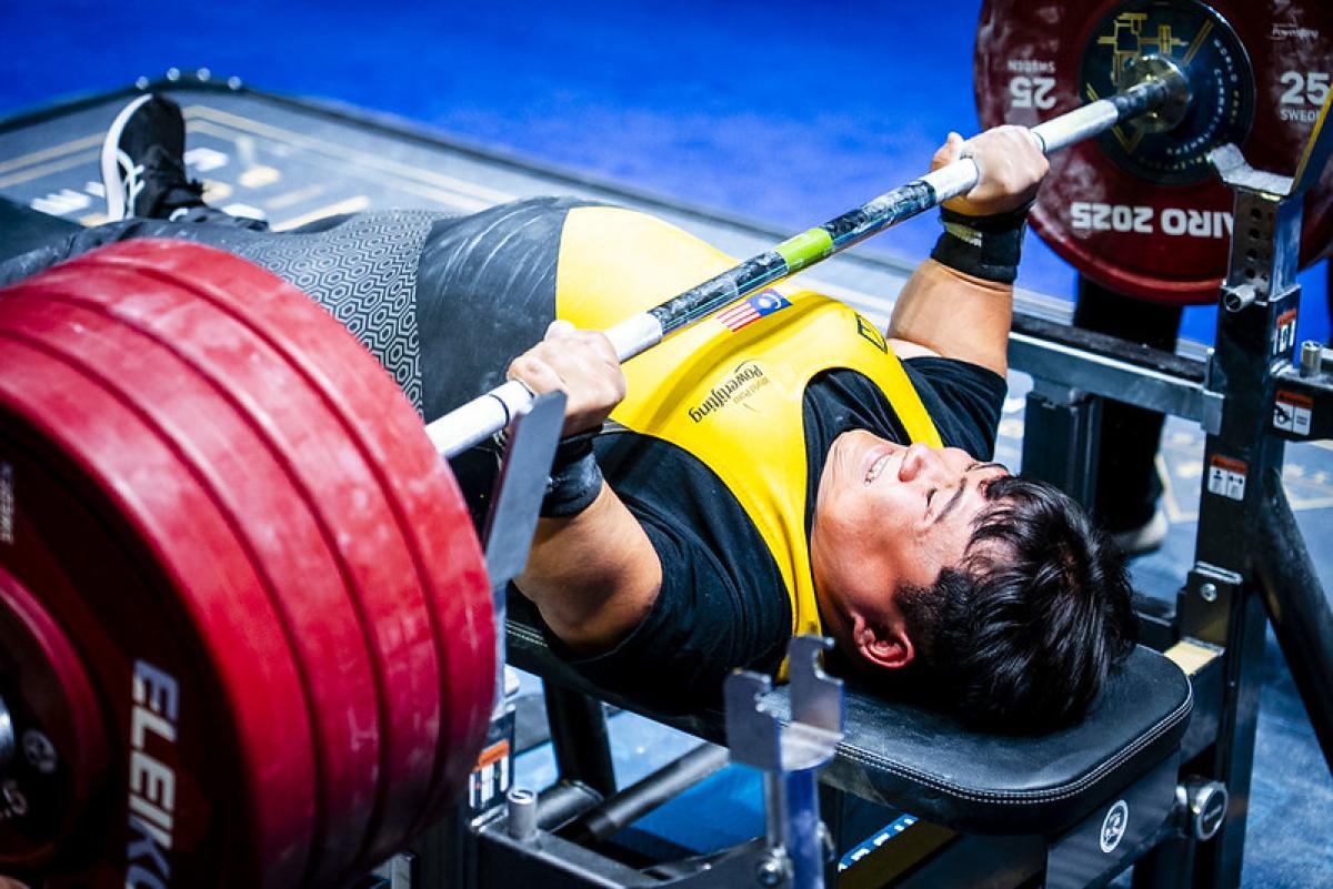 A short stature man lifting weight in a Para powerlifting competition
