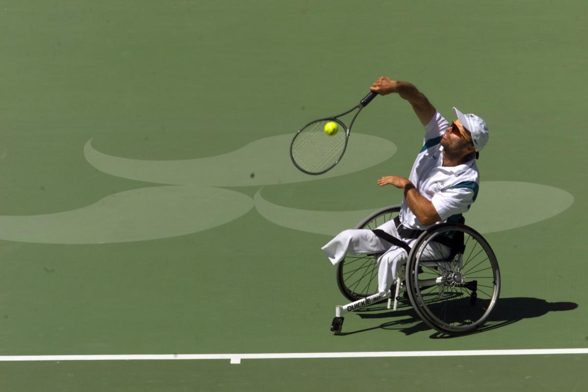A male wheelchair tennis player is in competition on a grass court