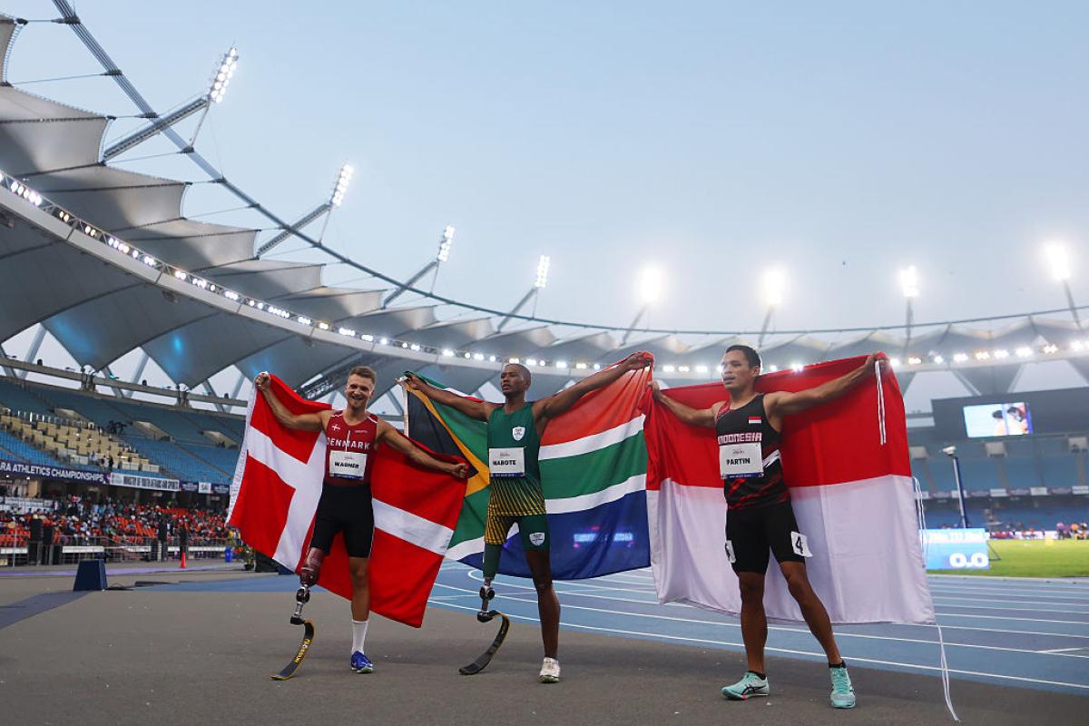 Three athletes with prosthetic legs with their country flags