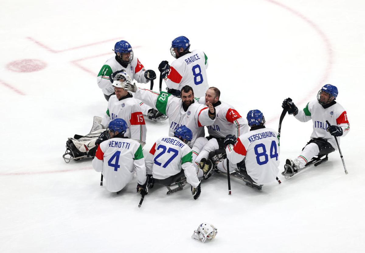 Nine Para ice hockey players wearing Italy's white jersey are celebrating on ice