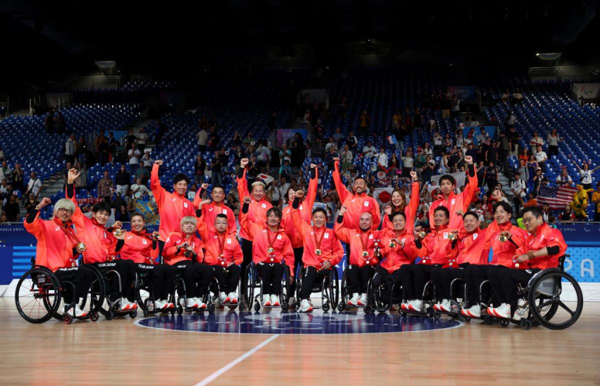 Eighteen wheelchair rugby players and officials wearing a red jersey pose for a photograph after receiving gold medals