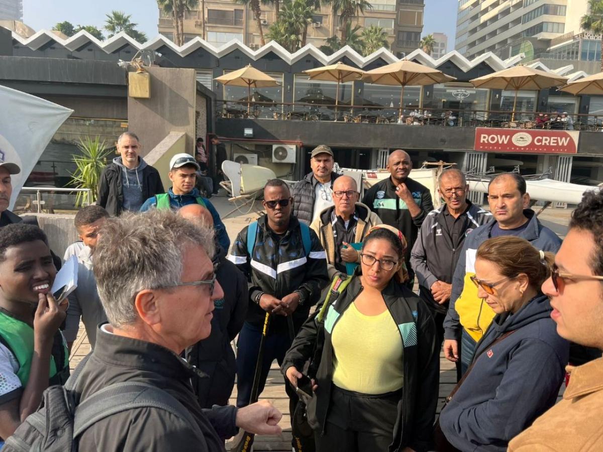 Fourteen men and woman gather around a male speaker during an outdoor seminar