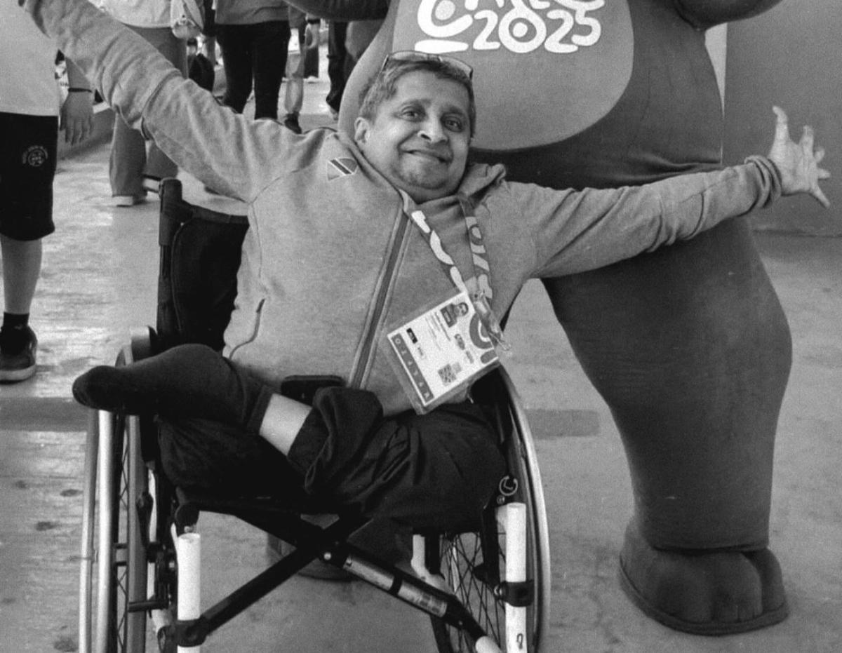 A male official wearing an accreditation is opening his arms wide to pose for a photo