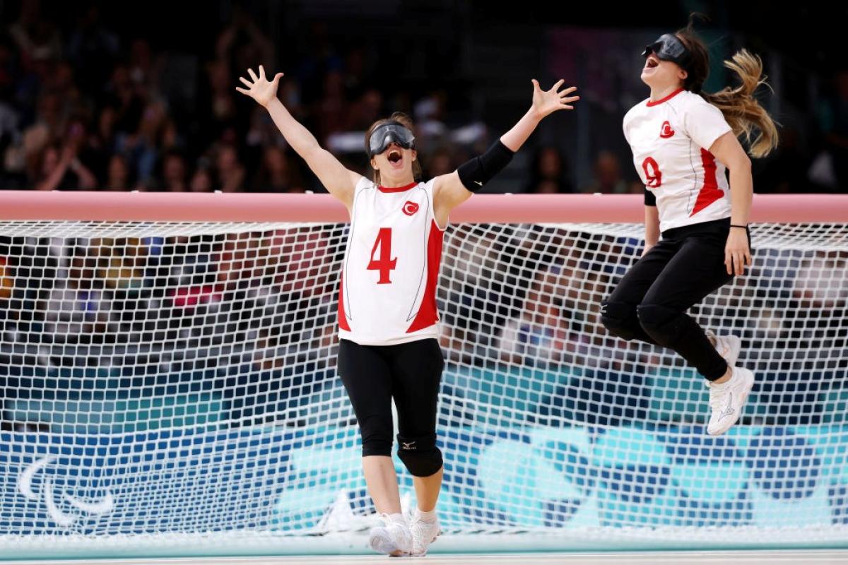 Two female goalball athletes celebrate in front of a net