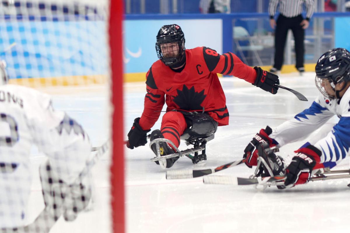 A male Para ice hockey player is scoring a goal