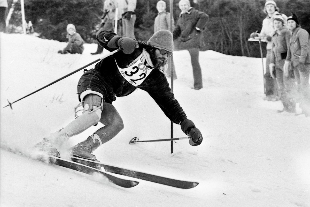 A black and white photo of a male athlete wearing a prosthetic leg is skiing downhill