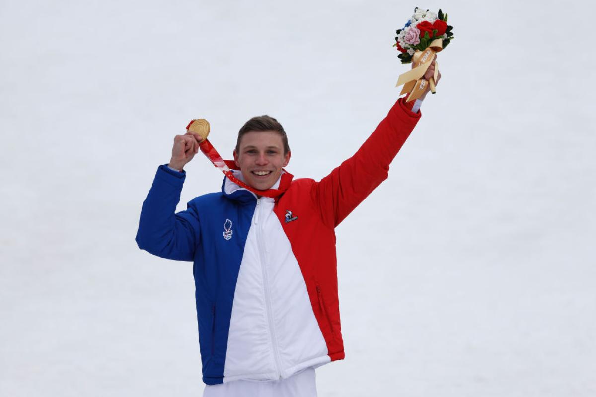 A male athlete wearing France's blue, white and red uniform celebrates on the podium at the Beijing 2022 Paralympics