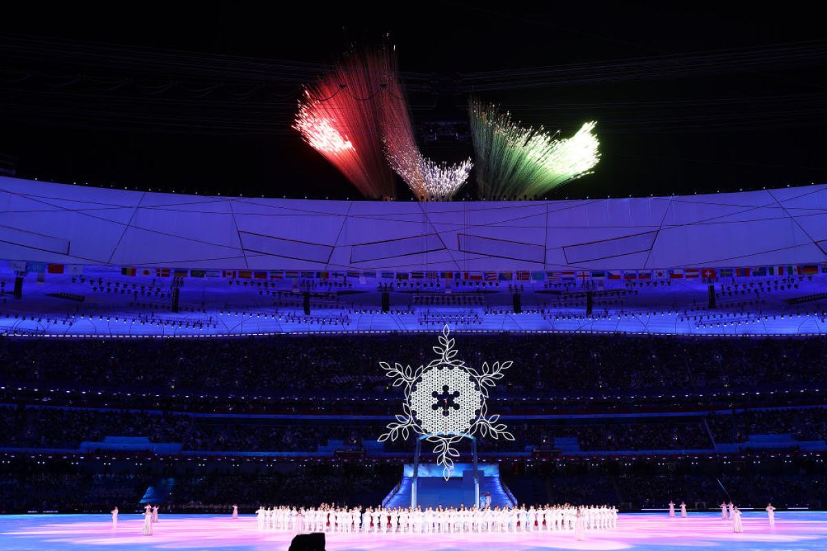 Fireworks in colours of red, blue and green shaped like the Paralympic symbol are lit above a stadium