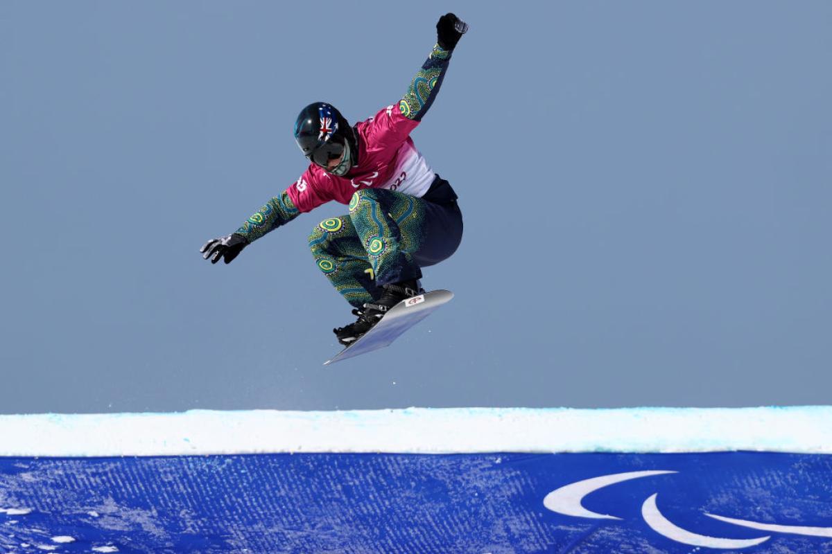 A male Para snowboard athlete is making a jump during the Beijing 2022 Paralympics