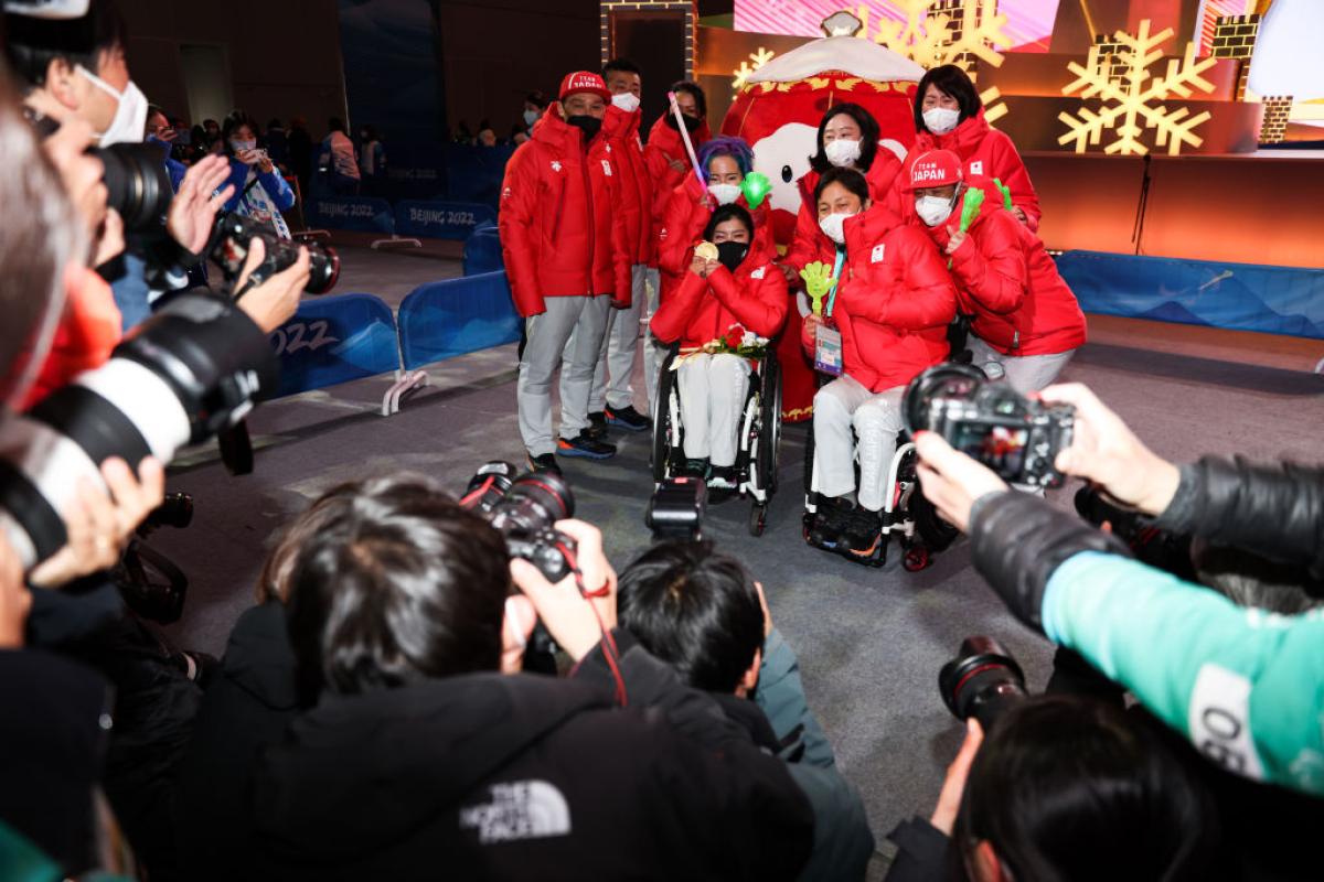 Nine athletes and officials from the Japanese delegation pose for a group photo in front of photographers at Beijing 2022