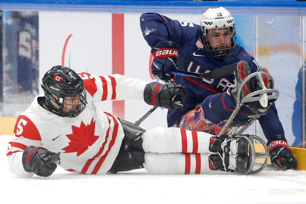 A male ice hockey player in white clashes with another male player in blue