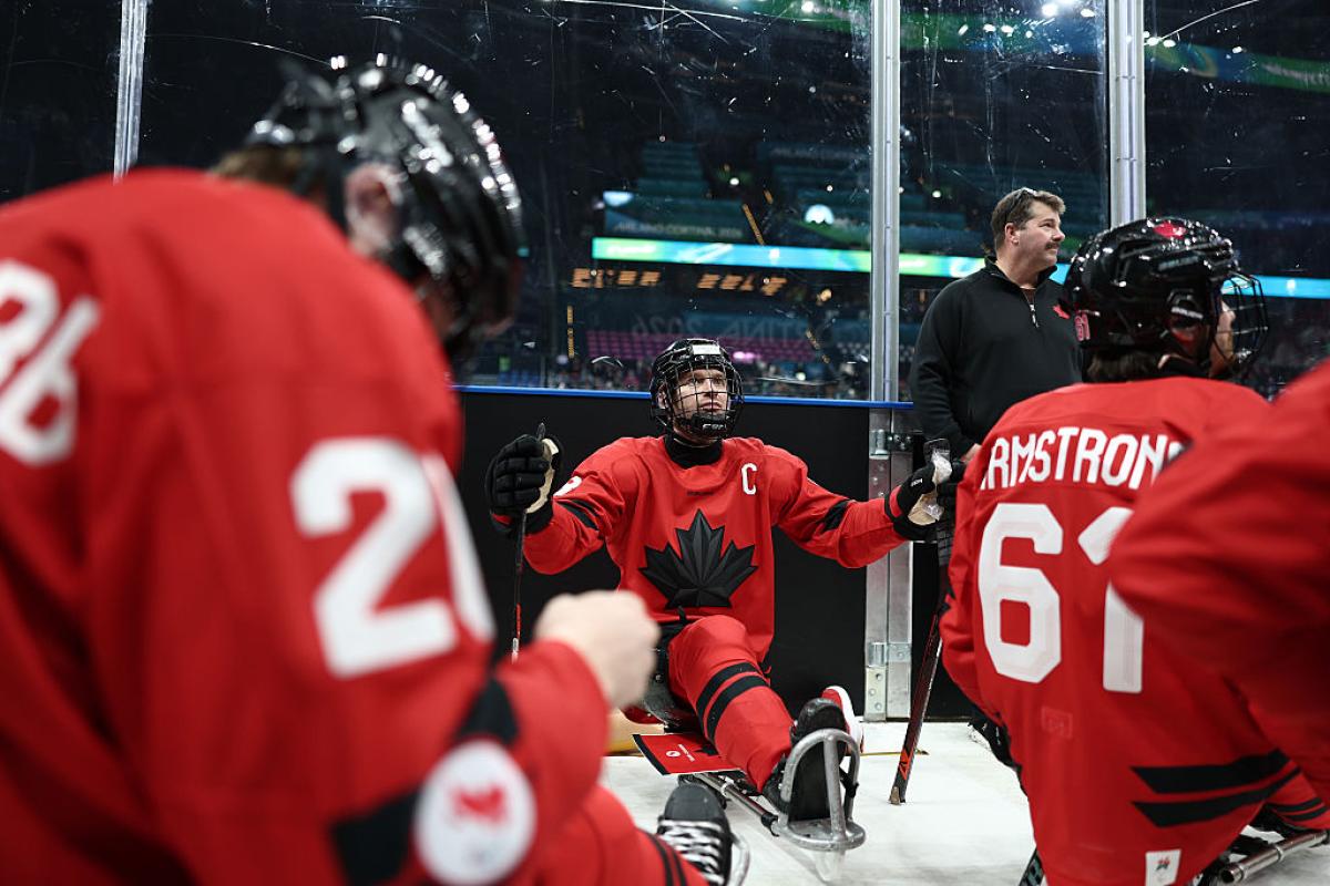 A Canadian Para ice hockey player between his teammates outside a rink