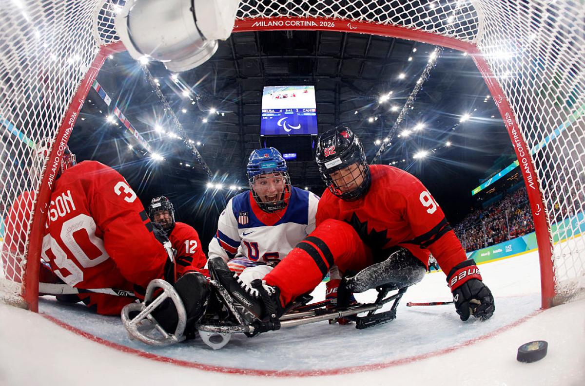A USA Para ice hockey player watching the puck enter the net in the middle of Canadian players