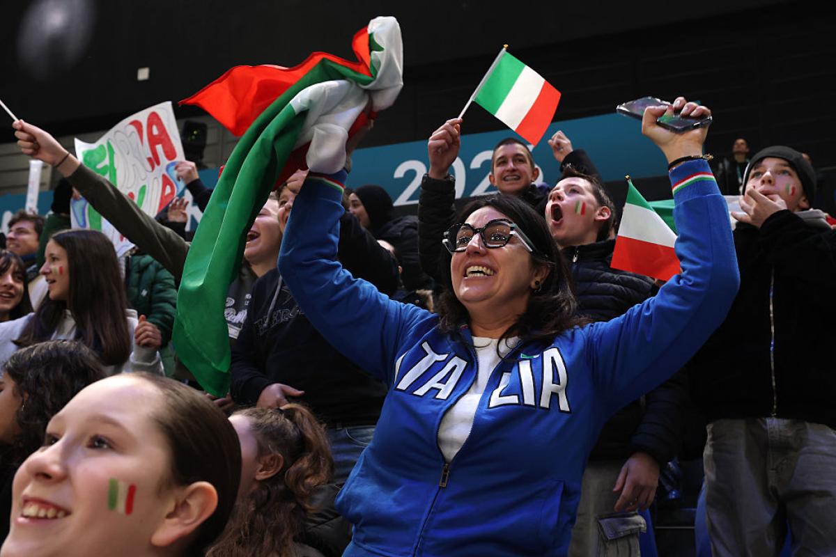 A group of fans waving Italian flags cheer in the stands