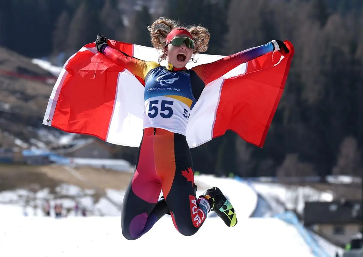 A female Para cross-country skier jumping while waving the Canadian flag