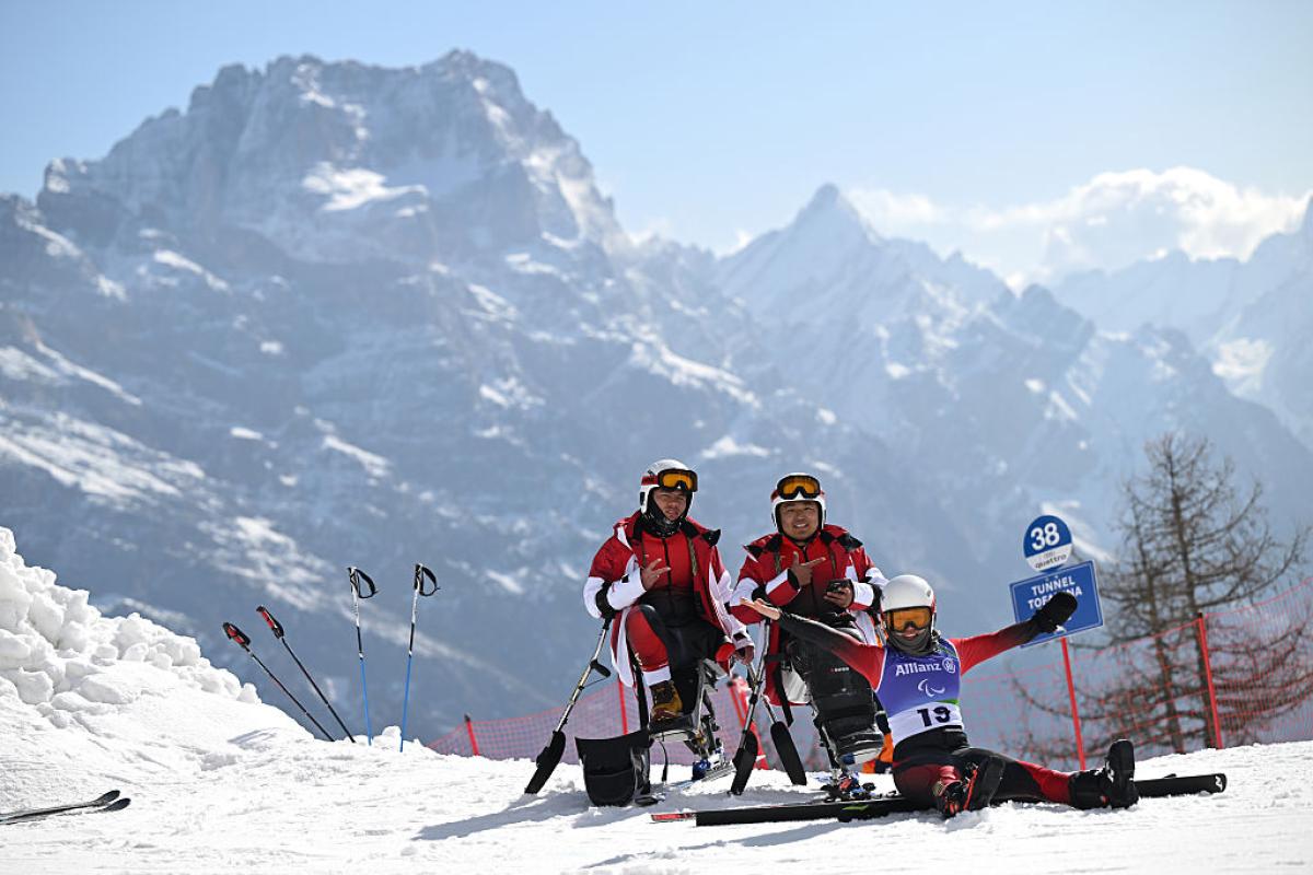 Three athletes pose for a photo in front of a snowy mountains