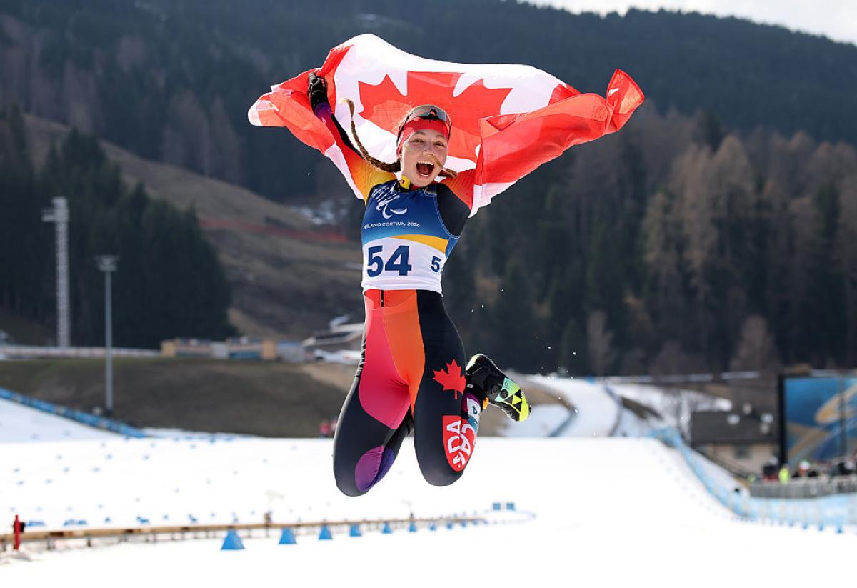 A female Paralympic skier is jumping while holding the Canadian flag