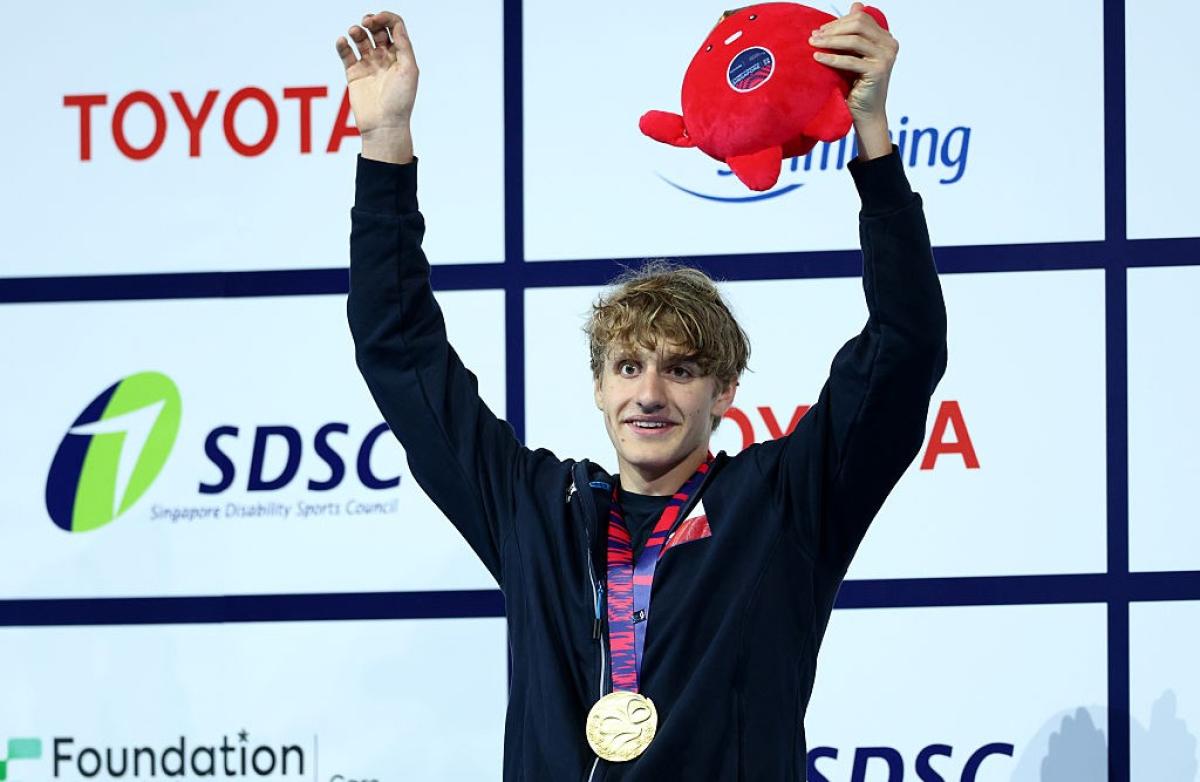 A young male athlete with open arms celebrating with a gold medal 