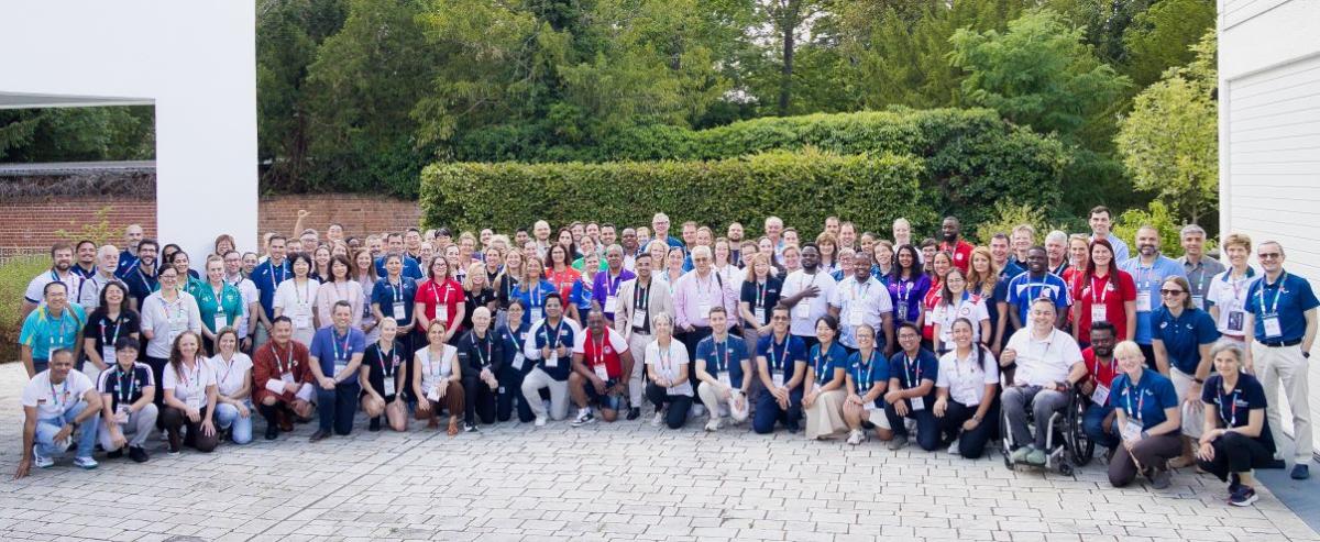 A group of around 100 people pose for a group photo outside