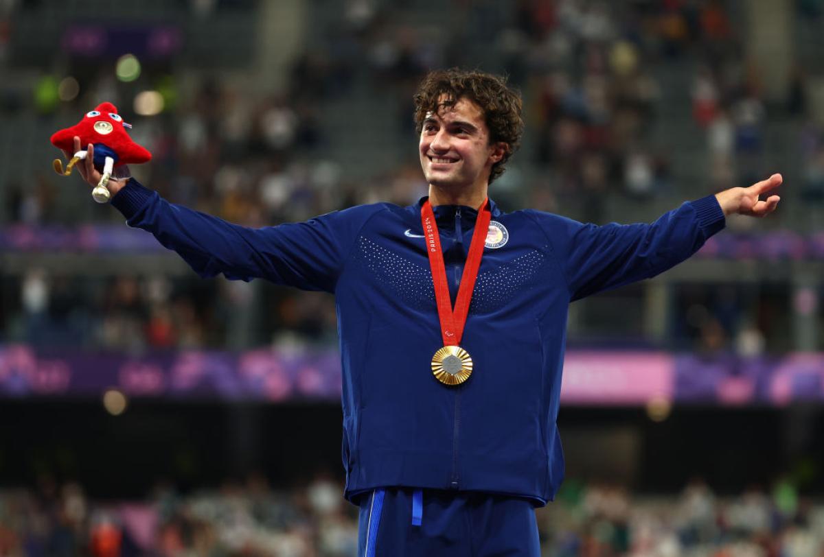 A male athlete with his gold medal and holding the Paris 2024 mascot in his right hand