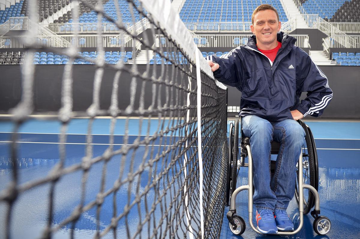 A picture of an athlete in a wheelchair next to a tennis let.