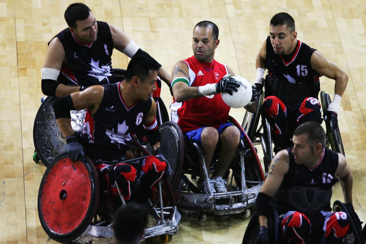 Troye Collins defending the ball between four Canadian players A picture of a person in a wheelchair trying to make a pass between four other person in a wheelchair.