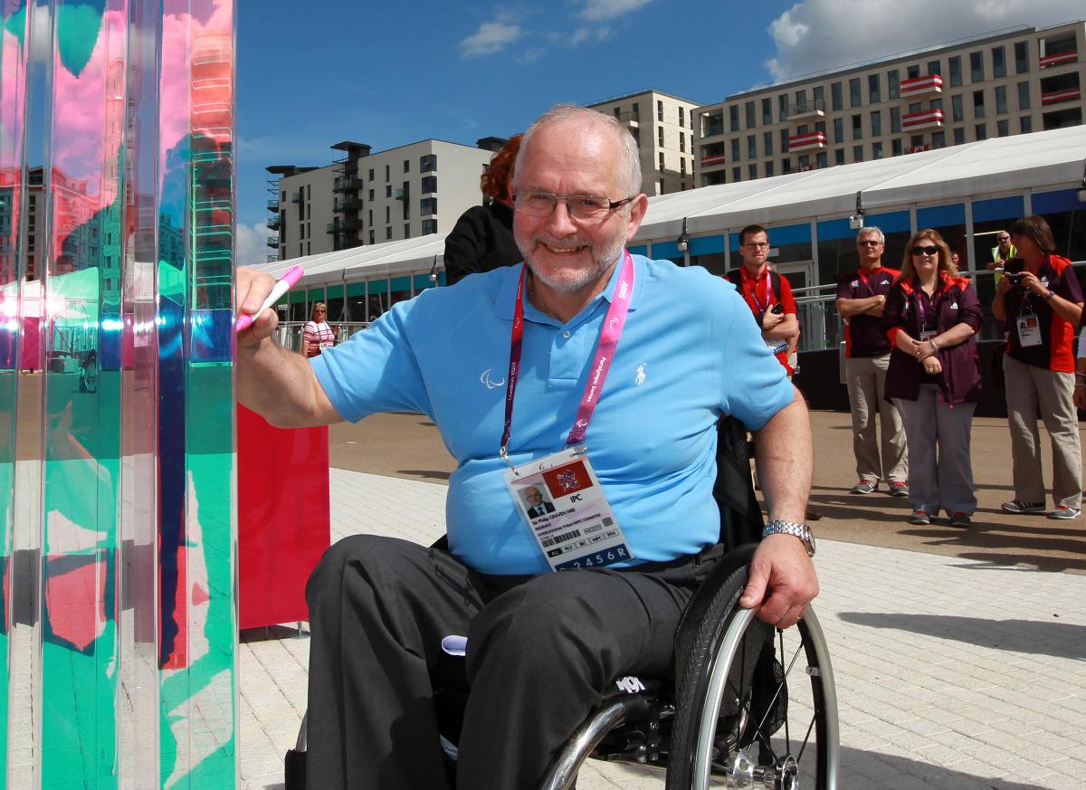 A picture of a man in a wheelchair signing a wall