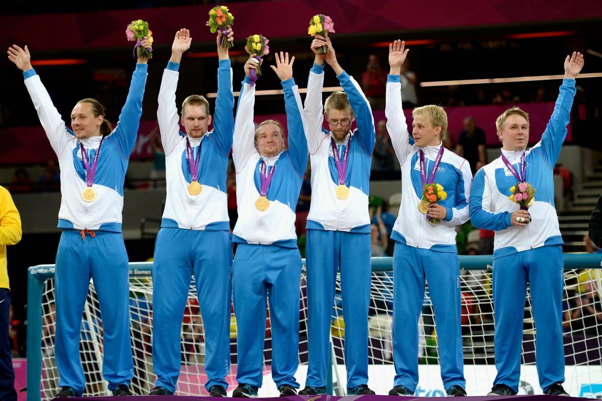 Finland goalball men's Six men in training suits standing in a row, waving and celebrating