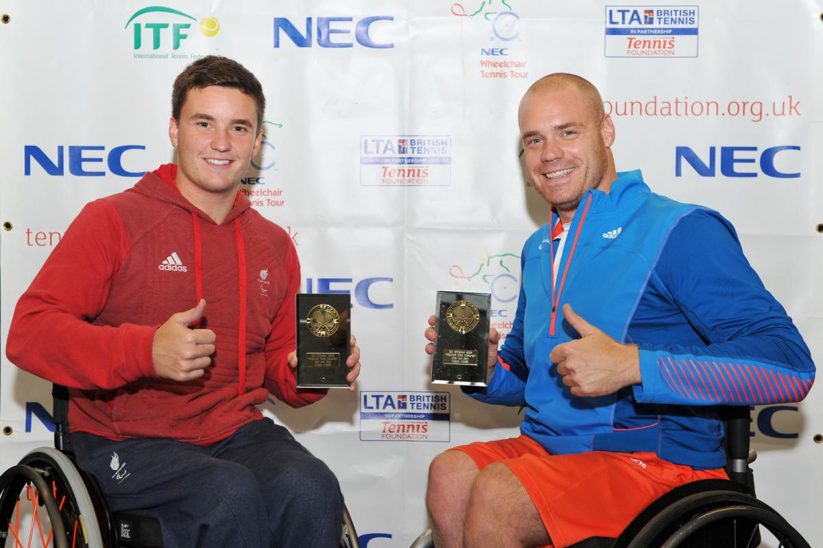 A picture of 2 men in a wheelchair showing their trophies