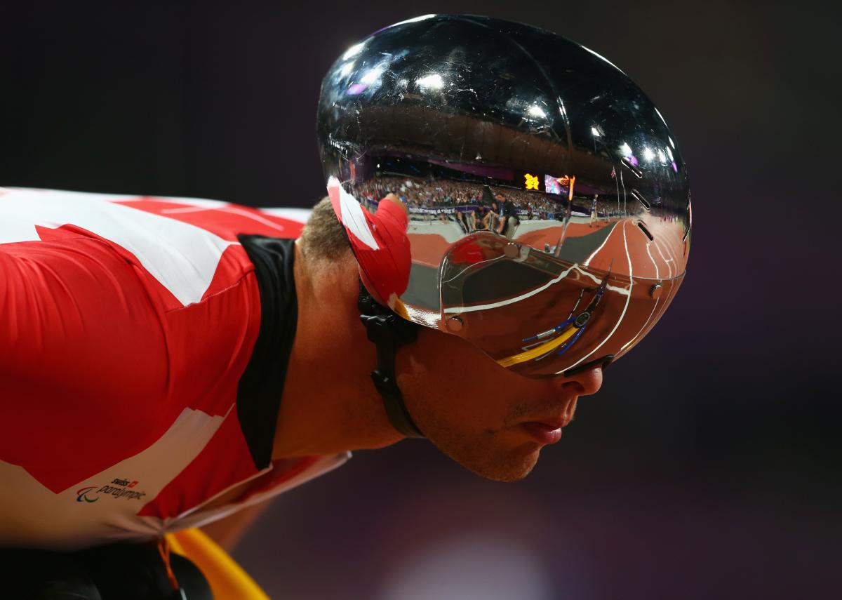 A man with a silver helmet and red jersey leans forward on his racing wheelchair