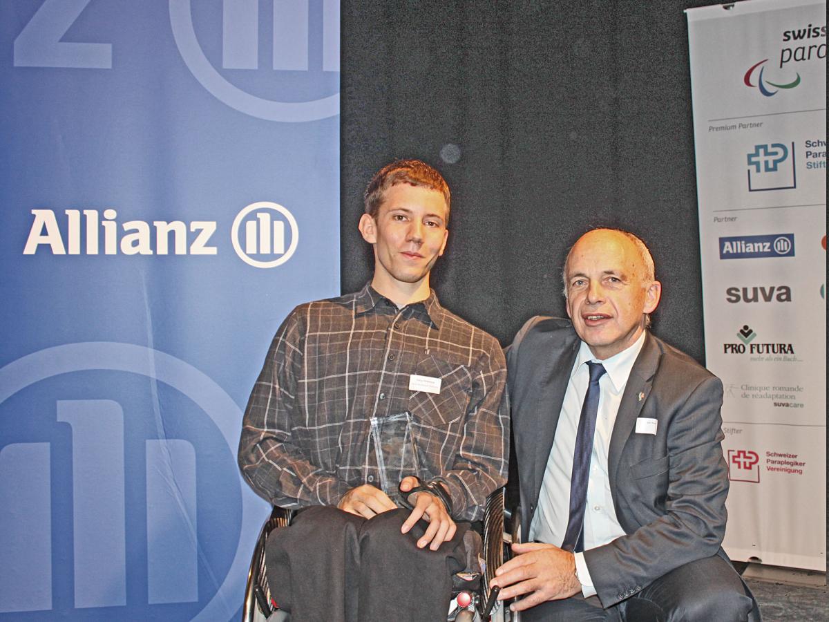 A picture of a man in a wheelchair posing with his award