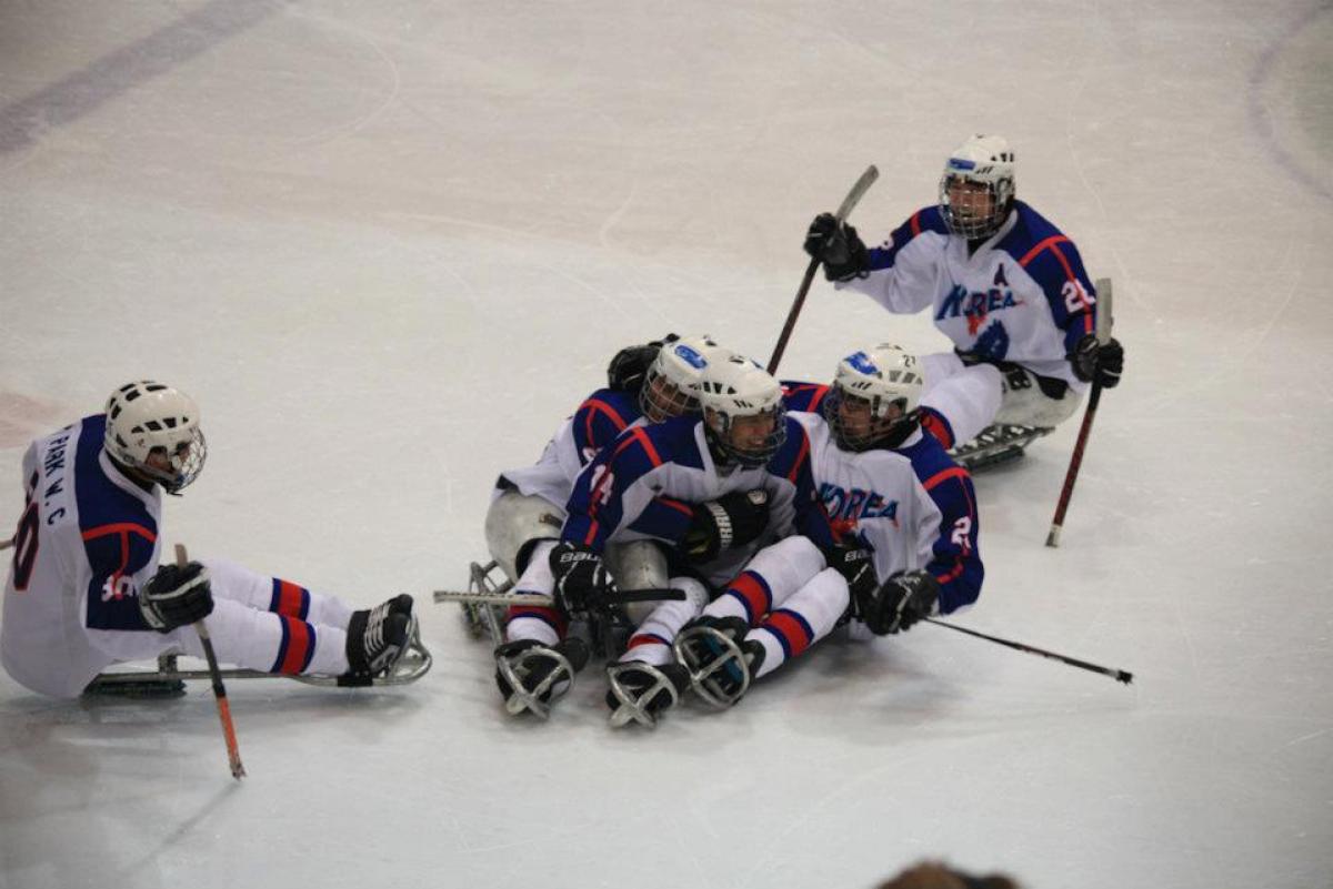 Korea Ice Sledge Hockey Team A picture of men sitting in a sledge celebrating their victory in a hockey match.