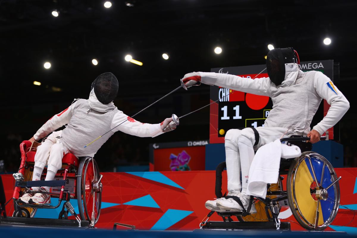 A picture of 2 men in wheelchairs fencing.