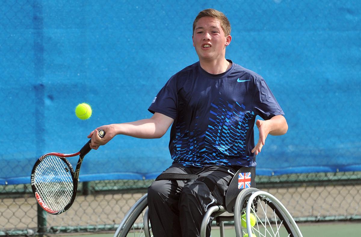 A picture of a young man in a wheelchair playing a forhand in a wheelchair tennis match
